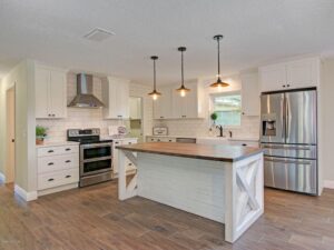 White kitchen under construction with white island sink, diagonal wood paneling, and copper range hood.