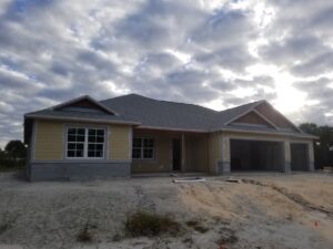 Newly constructed single-story house with gray roof, white walls, red garage door, and covered porch.