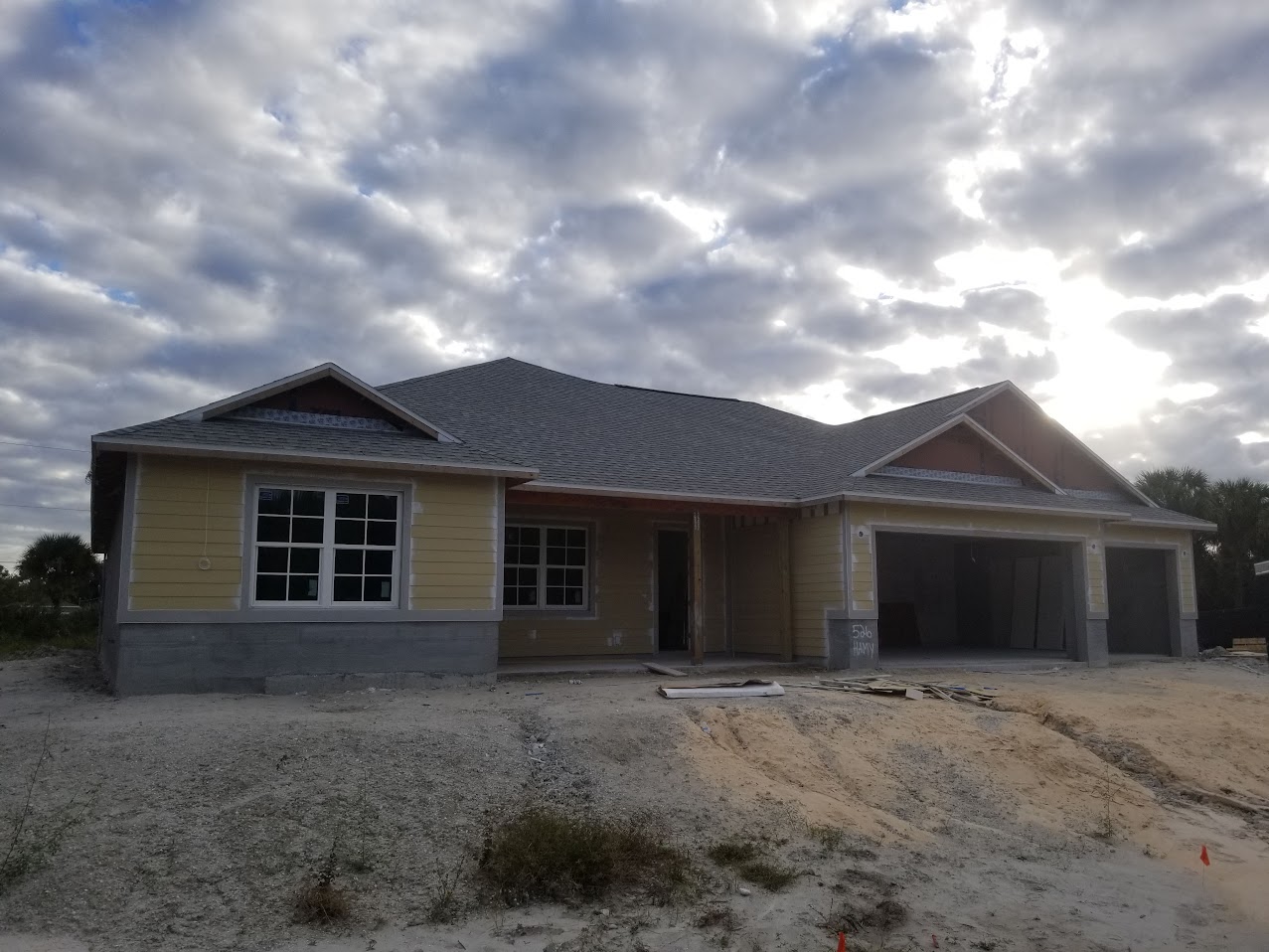 A newly constructed single-story house with a gray roof, white walls, two-car garage, front porch, and construction worker on the roof.